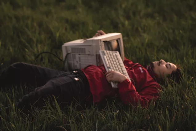 Photo of a person laying on the grass with an old fashioned computer in their lap.